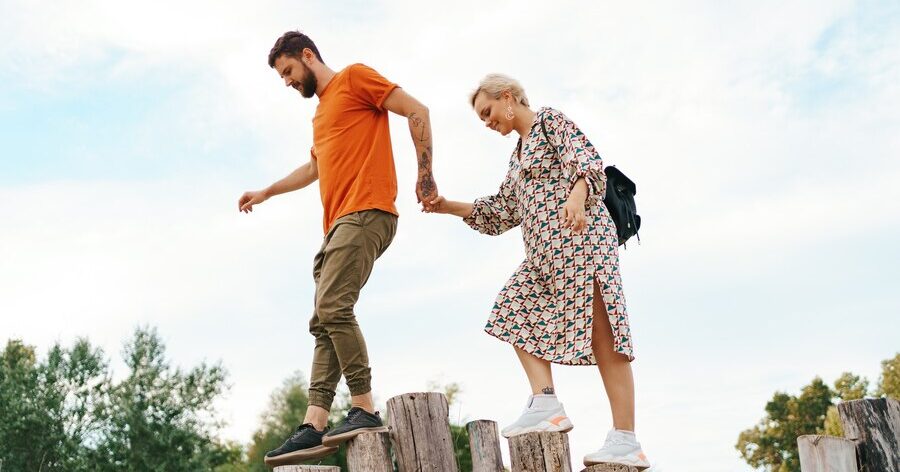 junges Paar balanciert über Holzpfähle bei einem Spaziergang durchs Grüne