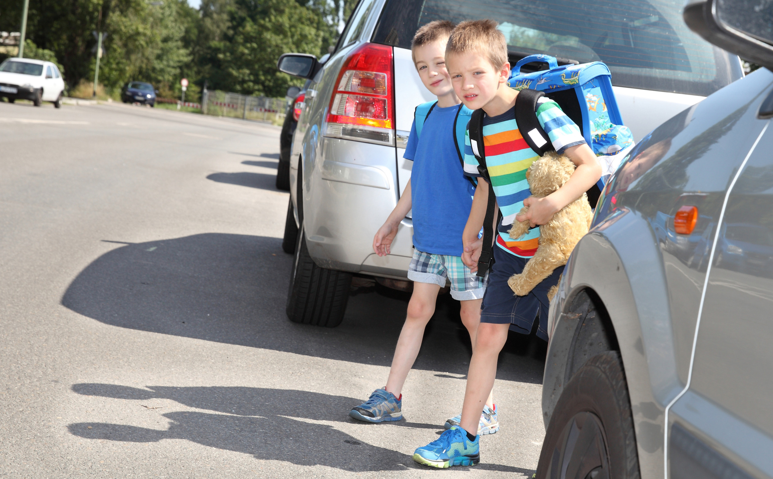 Zwei kleine Kinder zwischen parkenden Autos versuchen die Straße zu überqueren