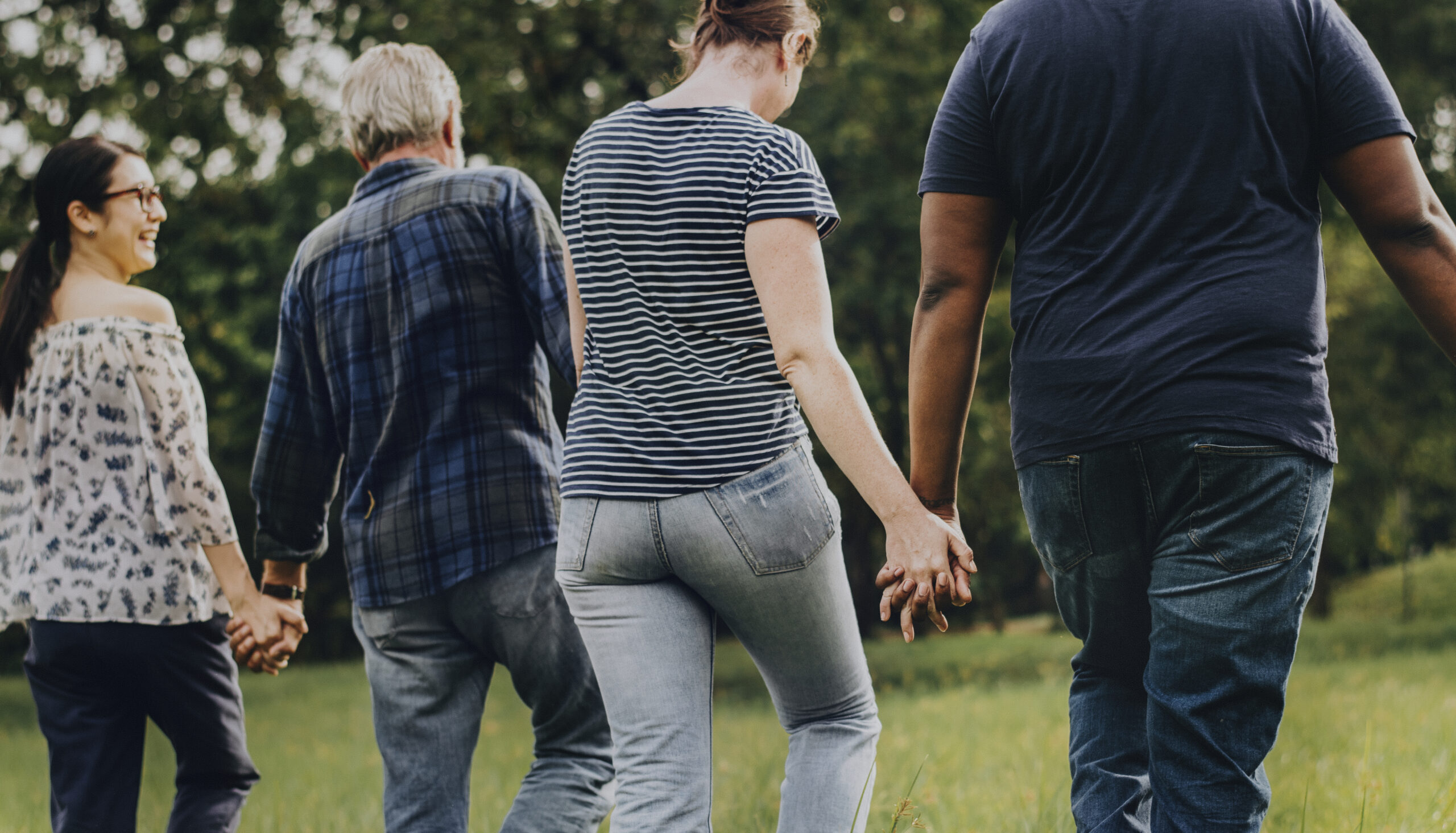 Diverse Menschen halten sich an den Händen und gehen durch einen Park